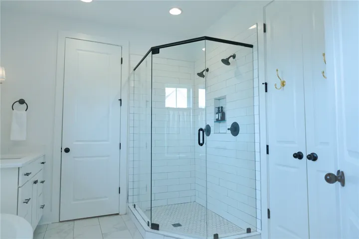 Modern bath features a large glass-enclosed shower with subway tile, multiple showerheads, and a built-in niche for essentials.