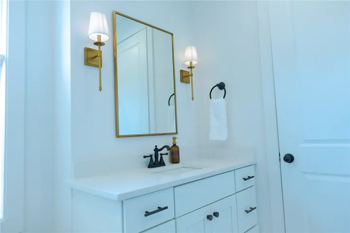 A well-lit bathroom with a white vanity, a sleek rectangular mirror, and elegant wall sconces.