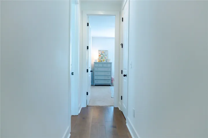 A well-lit hallway with rich wood flooring leads into a cozy bedroom space.