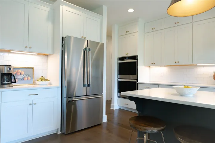 A gourmet kitchen boasts bright white cabinetry and rich hardwood flooring, centered around an inviting island with counter seating.