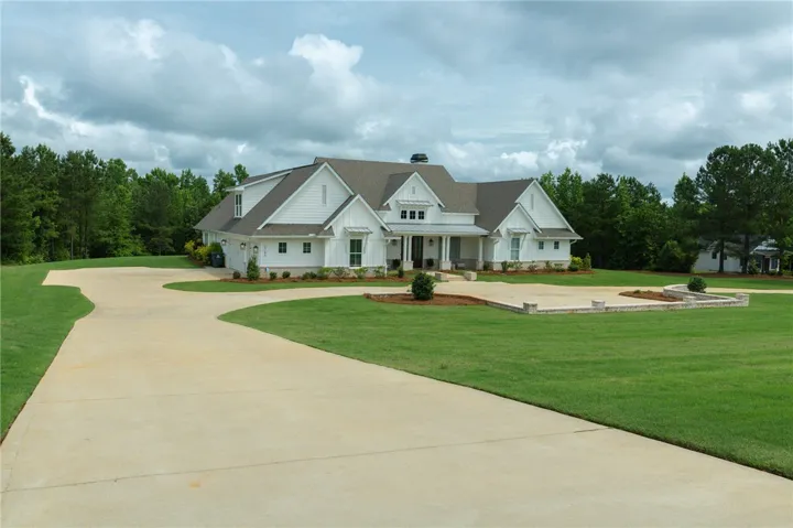A graceful driveway sweeps toward this elegant modern farmhouse, set against a backdrop of lush green landscaping and mature trees.