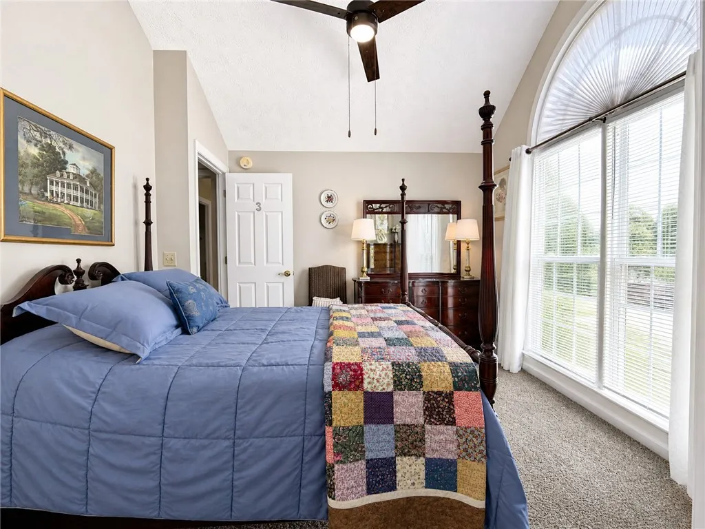 An inviting bedroom with vaulted ceilings and ample natural light from the large arched window.