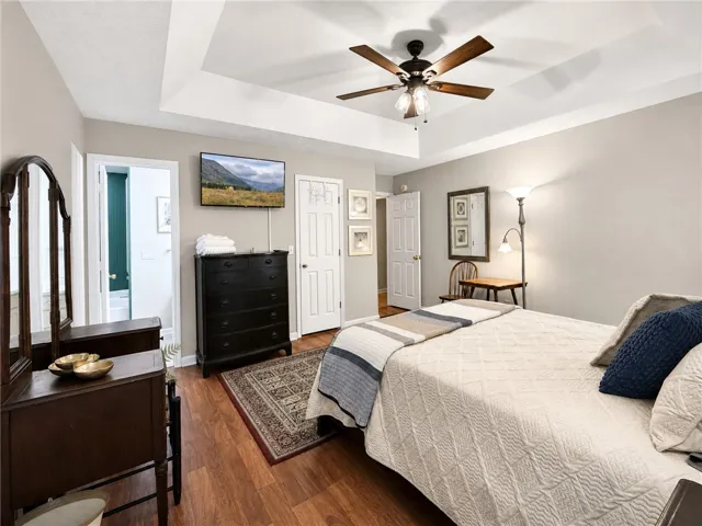 A well-lit bedroom features warm wood flooring and a classic ceiling fan.