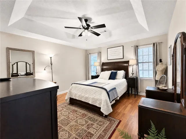Elegant tray ceilings and warm wood flooring define this comfortable primary bedroom retreat.