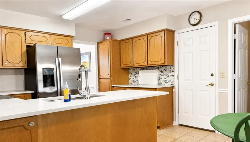 Bright, practical kitchen featuring a central island, stainless steel refrigerator, and ample cabinetry for storage.