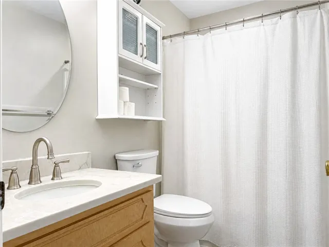 A pristine bathroom features a vanity with a white marble countertop and a glass-front storage cabinet above the toilet.