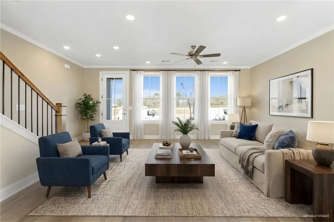 A generous living space with abundant natural light from a wall of windows and an elegant ceiling fan. Photos are not of subject property. Photos are of the same floorplan of a completed home.