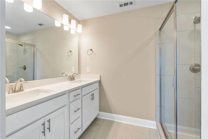 Dual vanity sinks and a spacious glass-enclosed shower create a functional, modern bathing space. Photos are not of subject property. Photos are of the same floorplan of a completed home.