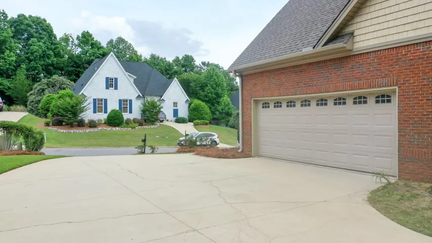 A classic brick garage with an arched window door complements the landscaped yard and distant homes.
