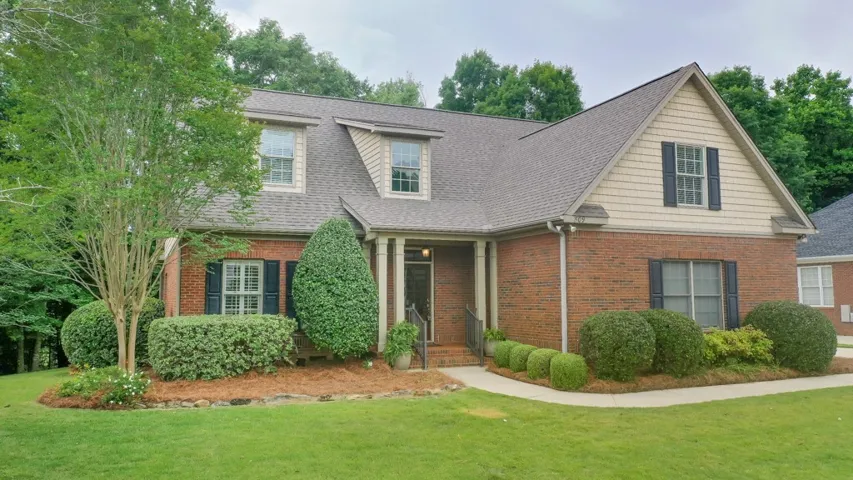 A classic brick-front residence featuring dormer windows and meticulously manicured landscaping.