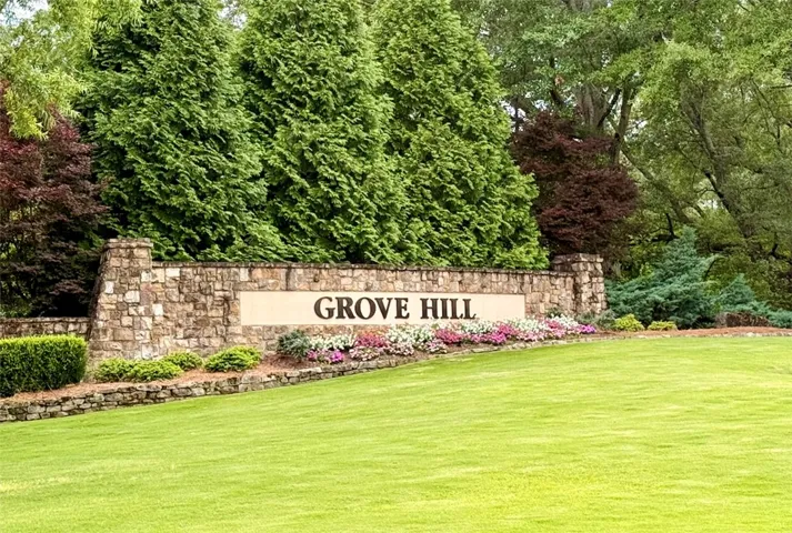 A welcoming stone monument entry features lush landscaping and verdant trees.
