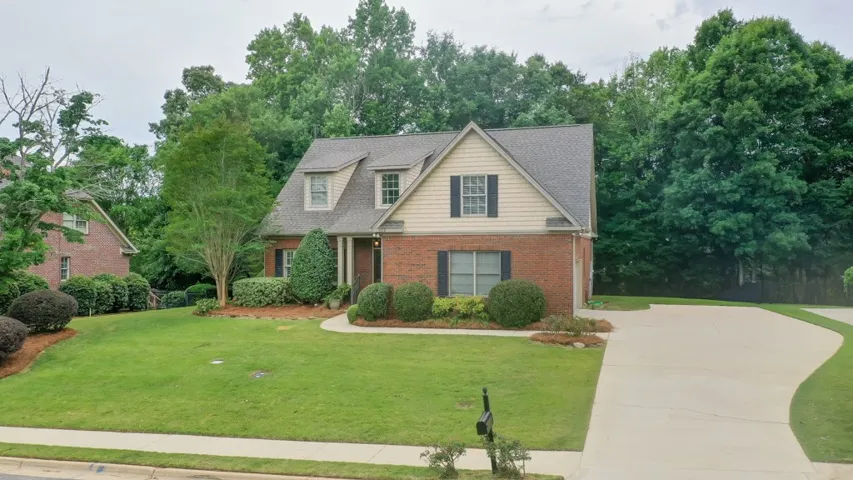 A classic brick-front home features dormer windows and a verdant, well-maintained lawn.