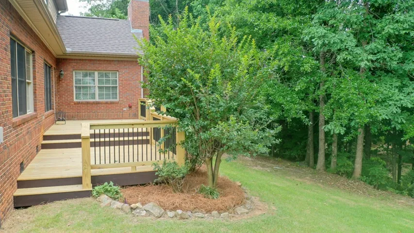 A new wooden deck extends from a classic brick home, surrounded by verdant trees and a well-kept yard.