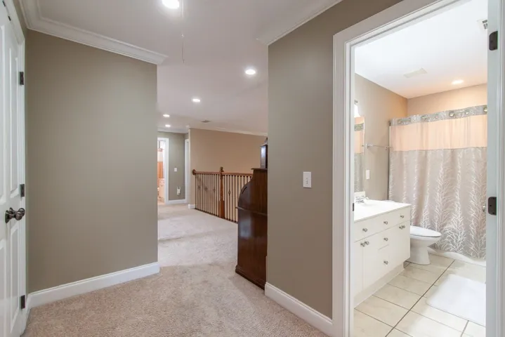 A well-lit landing features soft carpeting and crown molding, with a glimpse into a tiled bathroom.