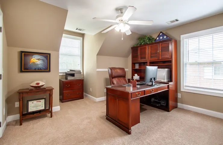 Well-lit office space features an angled ceiling and a practical ceiling fan.