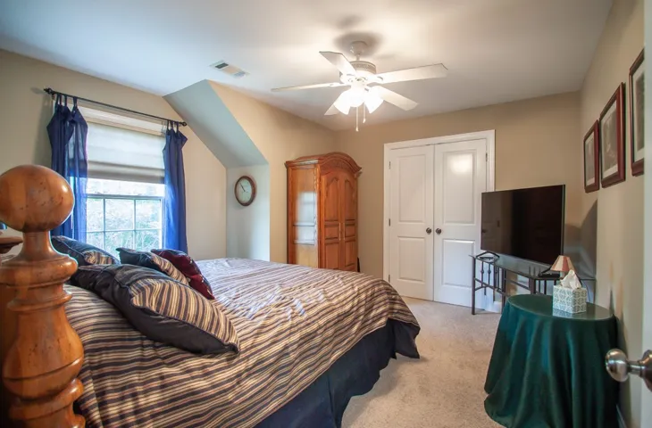 An inviting room features a functional ceiling fan, plush carpeting, and ample natural light from the large window.