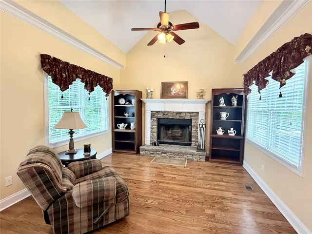 A comforting keeping room features a stone fireplace, high ceilings, and beautiful hardwood flooring.