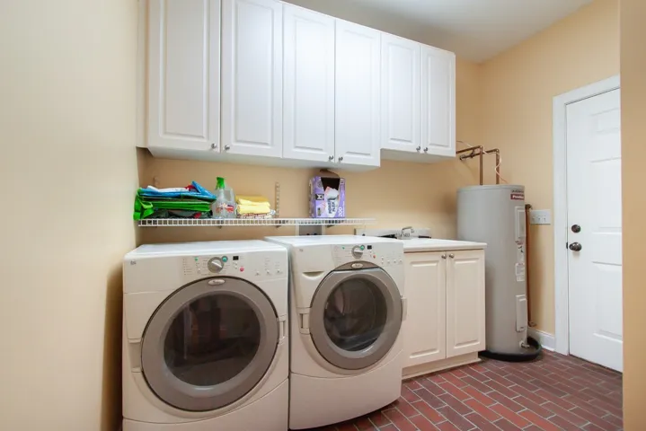 Functional laundry room featuring brick flooring, abundant cabinetry, and a convenient utility sink.