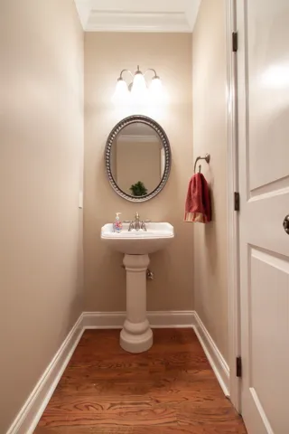 A well-lit powder room showcases rich wood flooring and a classic pedestal sink.