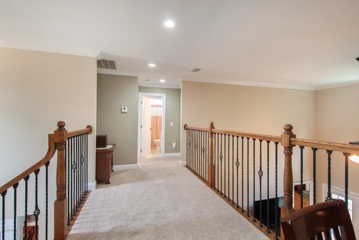 Carpeted upper-level landing with wrought iron and wood banisters, leading to another room with a tiled floor.