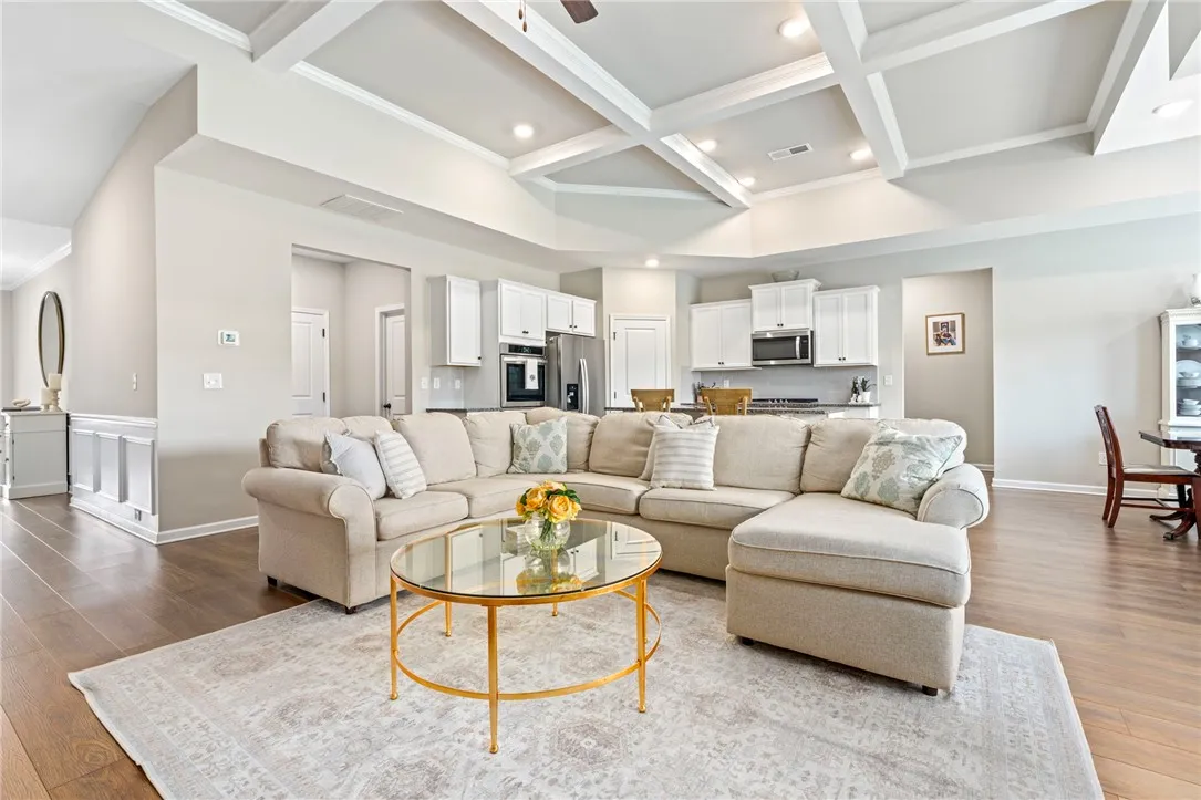 A well-lit great room features an open floorplan with coffered ceilings and rich hardwood flooring.