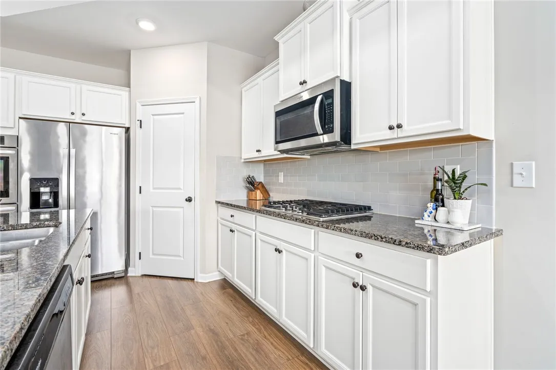 White cabinetry, granite counters, and wood flooring complement this well-appointed kitchen.