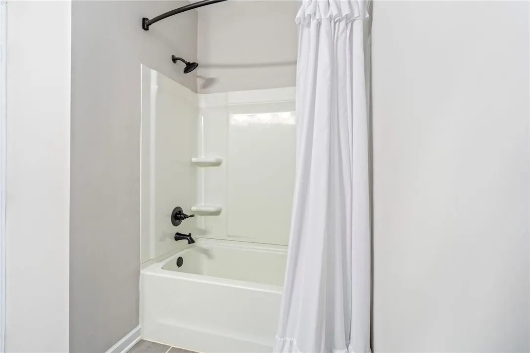 A pristine tub-shower combination with dark bronze fixtures and tiled flooring awaits.