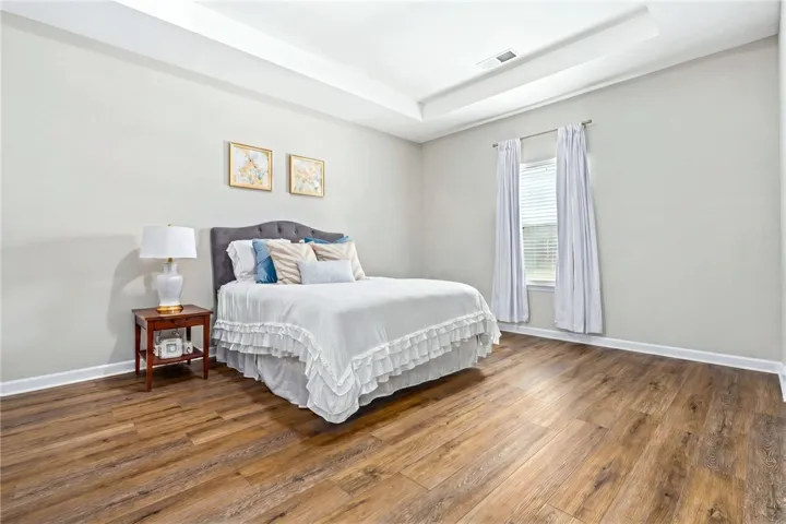 A restful bedroom offers generous space and warm wood flooring under a chic tray ceiling.