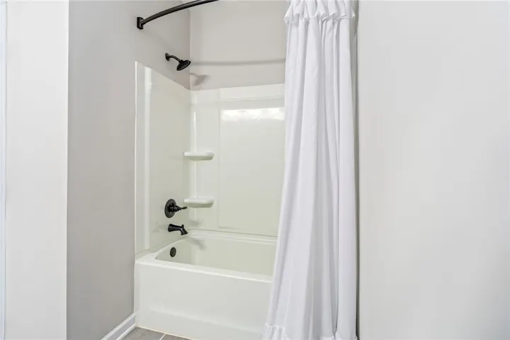 A pristine tub-shower combination with dark bronze fixtures and tiled flooring awaits.