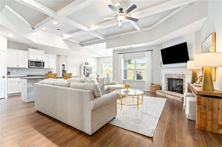 An inviting gathering space features an open-concept kitchen and a warm hearth, crowned by a coffered ceiling.