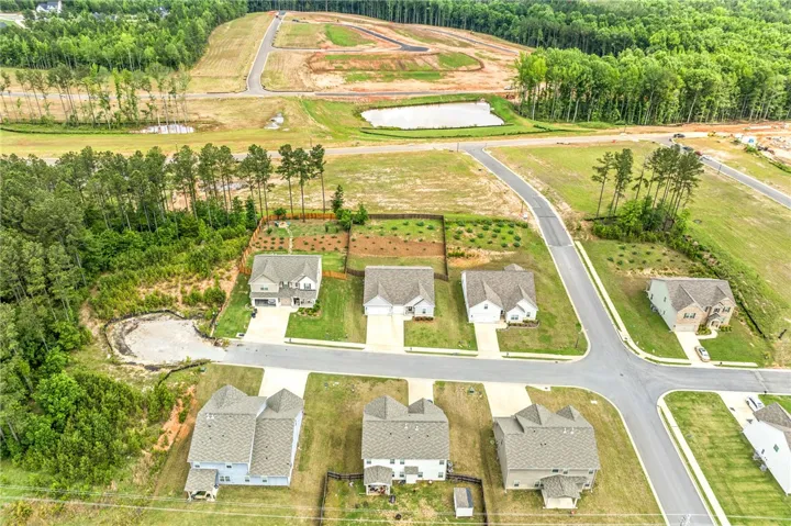 An aerial perspective reveals a developing neighborhood bordered by a tranquil wooded area and a peaceful pond.