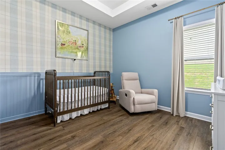 Warm wood-look flooring anchors this comfortable nursery, complete with decorative wainscoting and natural illumination.