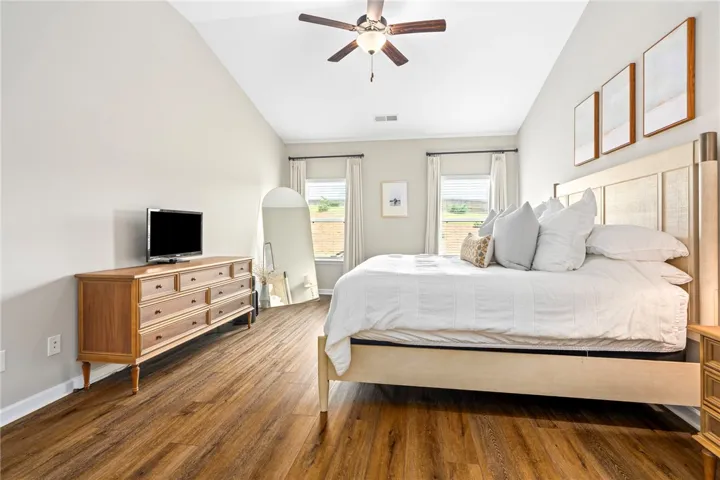 Natural light fills this spacious bedroom featuring warm flooring and a vaulted ceiling with a fan.