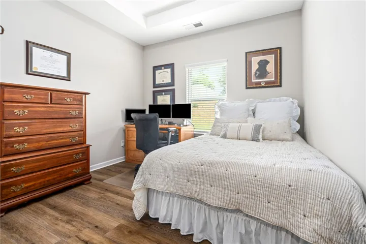 Well-lit room featuring rich hardwood flooring and a stylish tray ceiling, perfect for comfortable living.