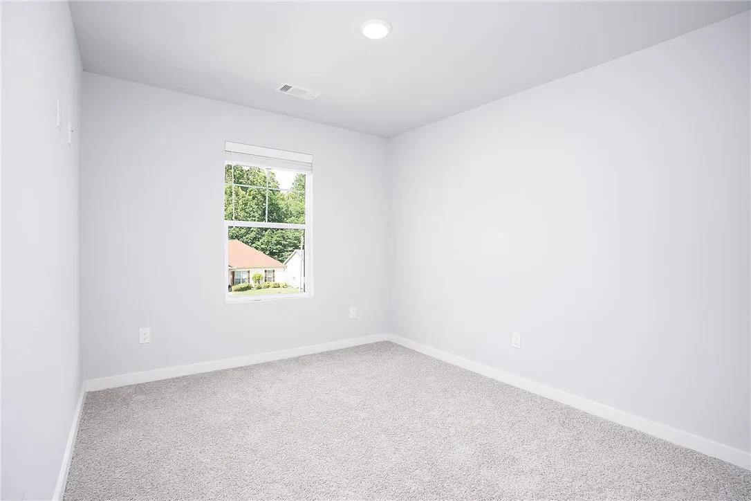 A well-lit, neutral-toned space features soft carpeting and a window overlooking lush greenery.
