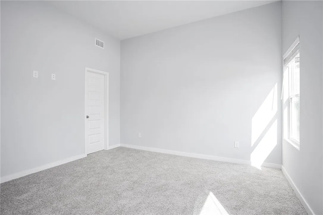 A well-lit room with soft carpeting, a clear window, and an accessible doorway.