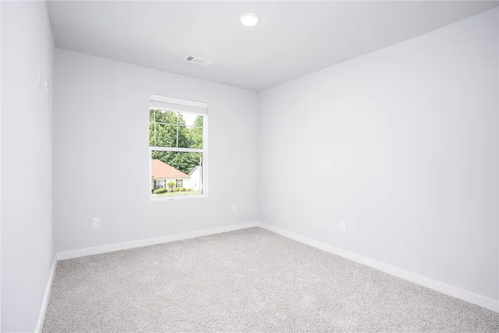 A well-lit, neutral-toned space features soft carpeting and a window overlooking lush greenery.