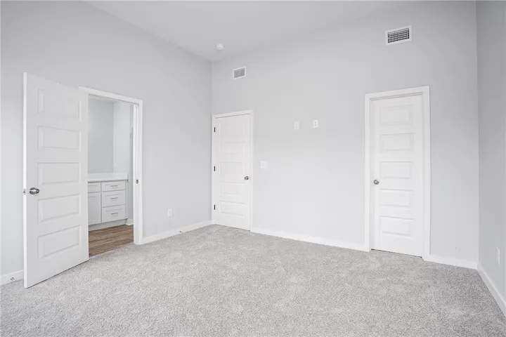 A spacious bedroom with plush carpeting leads to an adjacent room featuring wood flooring and white cabinetry.