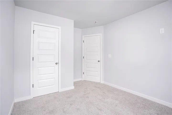 A spacious room awaits personalization, featuring two pristine white doors and soft, neutral carpeting.