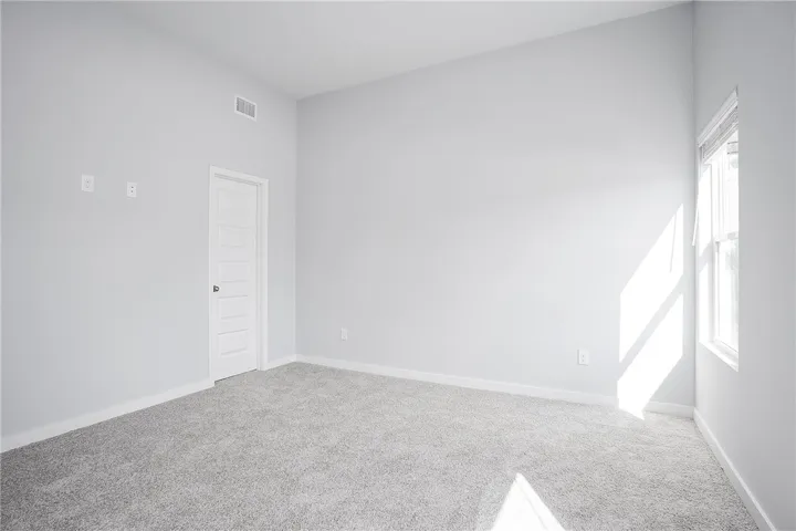 A well-lit room with soft carpeting, a clear window, and an accessible doorway.