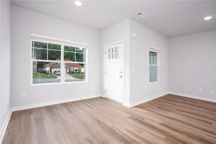 A sun-filled room offers modern wood-look flooring and a secure entry door.