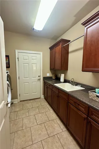 Functional laundry room offers extensive cabinetry, a built-in sink, and easy-care tile flooring.