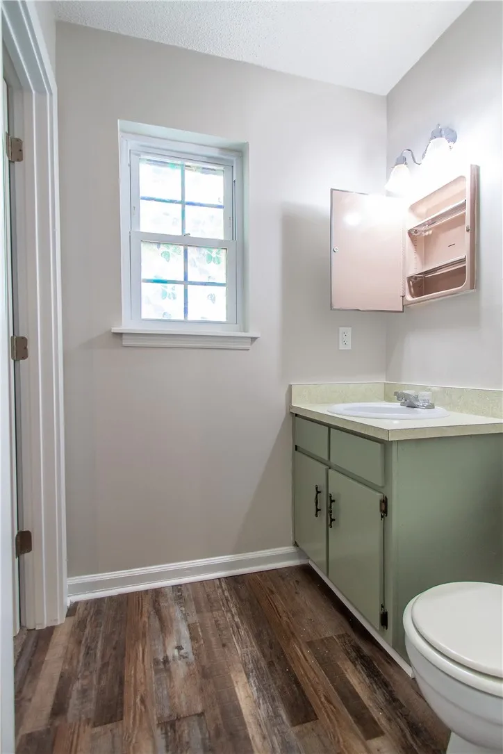 Bright, naturally illuminated bathroom with wood-style flooring and a window providing refreshing ventilation.