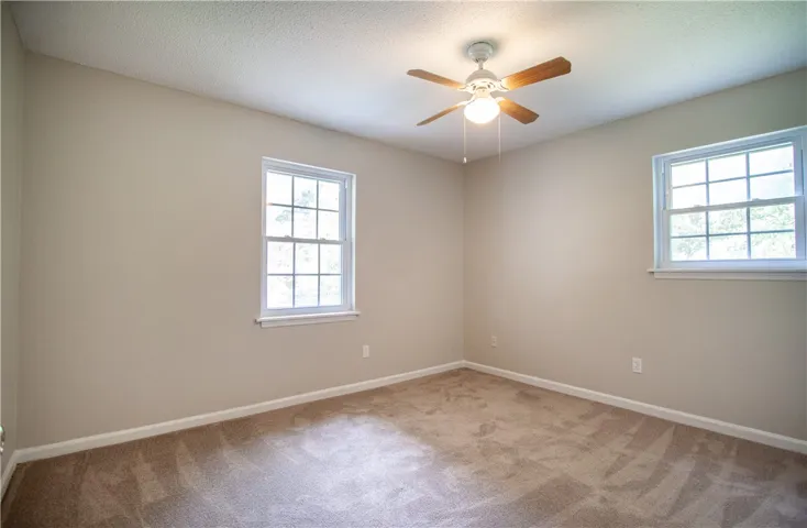 A quiet bedroom with ample natural illumination from multiple windows and soft carpeting.