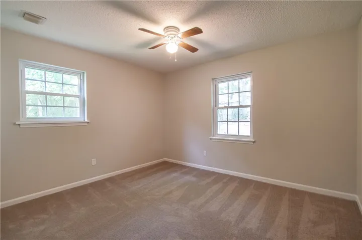 A well-lit bedroom features plush carpeting and a ceiling fan for year-round comfort.