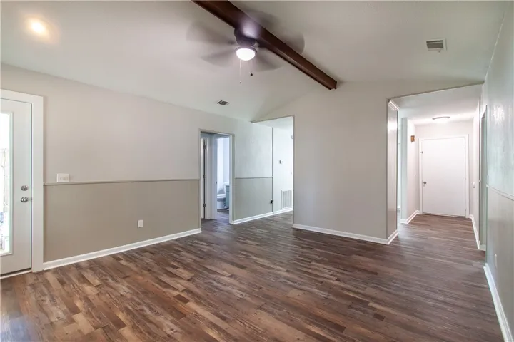 A living area with durable wood-look flooring and a functional ceiling fan, connecting to other rooms.