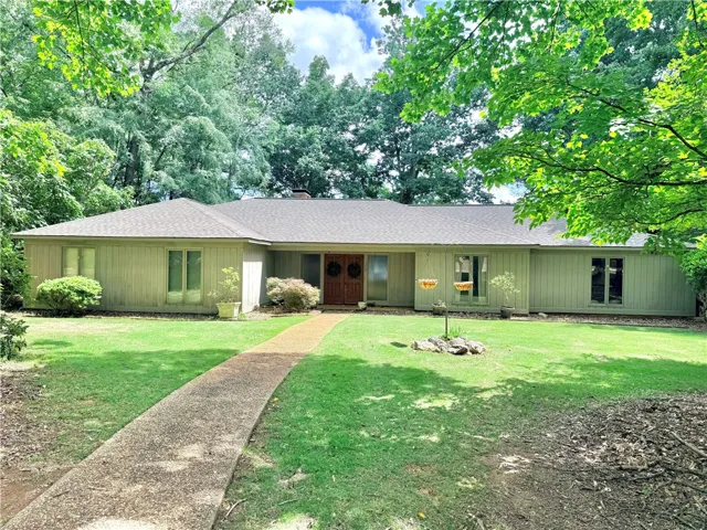 A winding path leads to this inviting residence, nestled amidst a lush green lawn and mature trees.