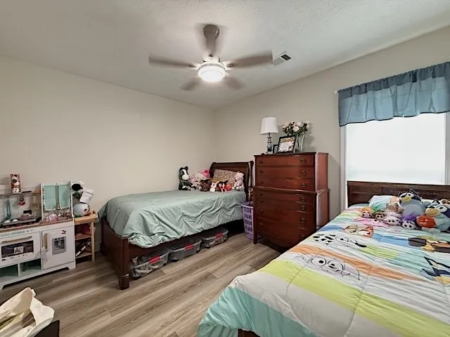 A well-lit bedroom featuring durable wood flooring and ample space for twin beds, offering comfortable living.