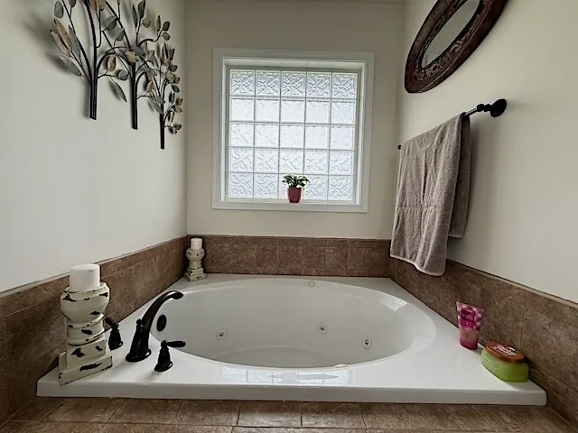 Relax in the deep soaking tub, illuminated by natural light from the patterned glass block window.