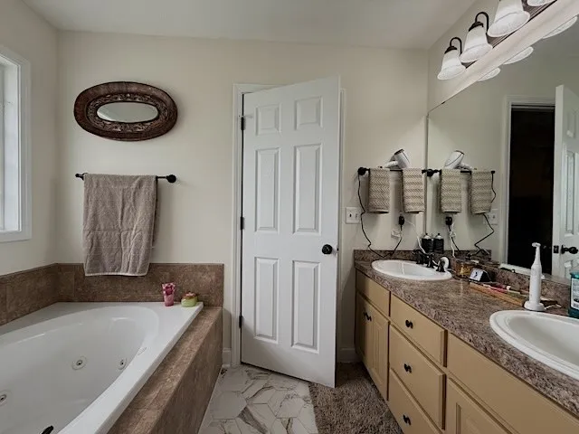 Relaxing jetted tub complements this well-appointed bath with dual vanities and tiled flooring.